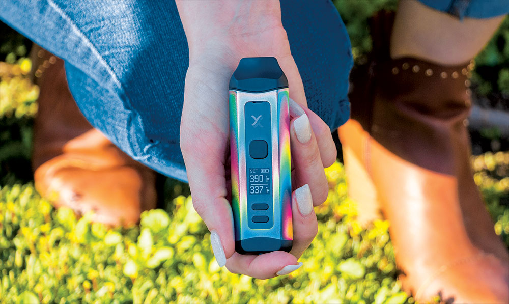 Hands holding a blue Exxus Mini Plus vaporizer outdoors