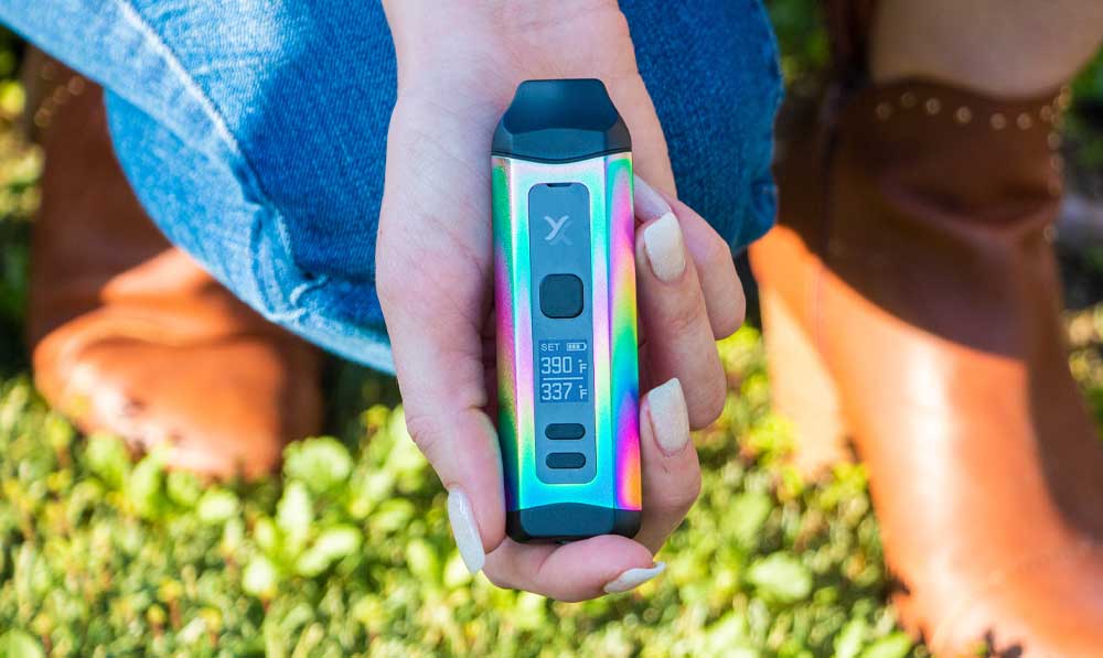 Hands holding a teal Exxus Mini Plus vaporizer over grass