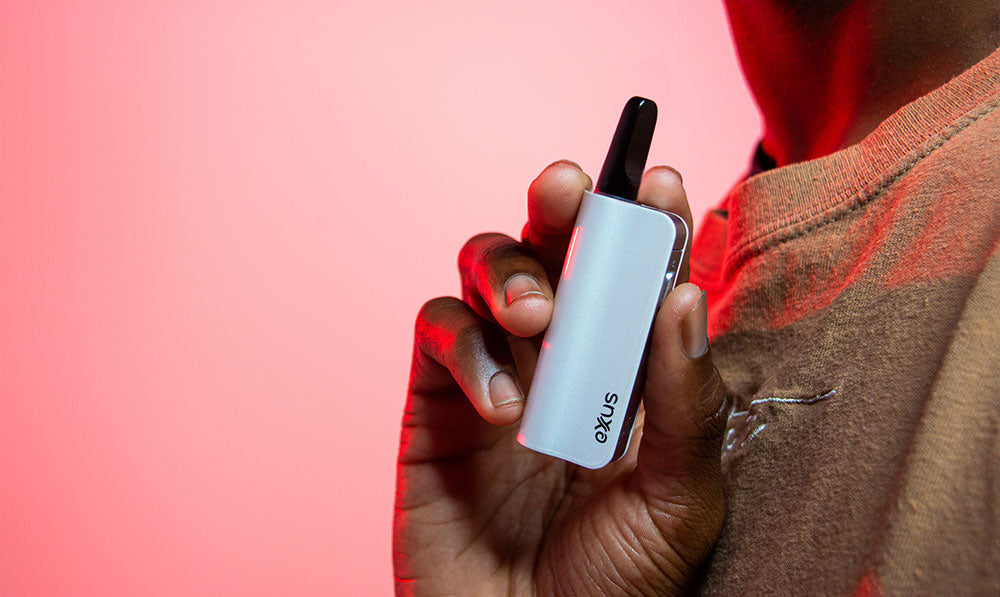 Hand holding a white Exxus Snap VV Mini against a pink background