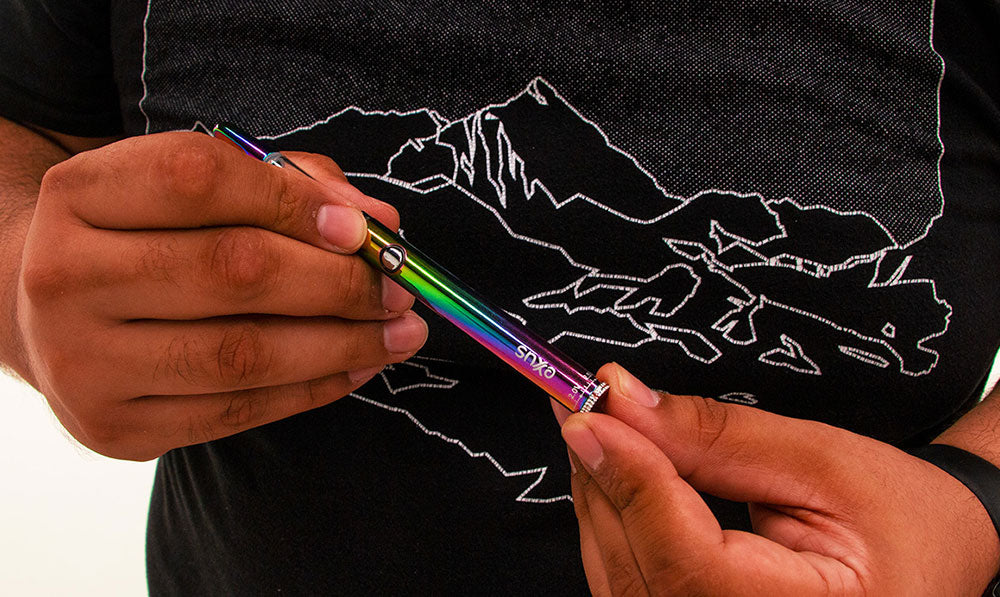 Hands holding a rainbow Exxus Twistr 510 thread battery with a cartridge attached
