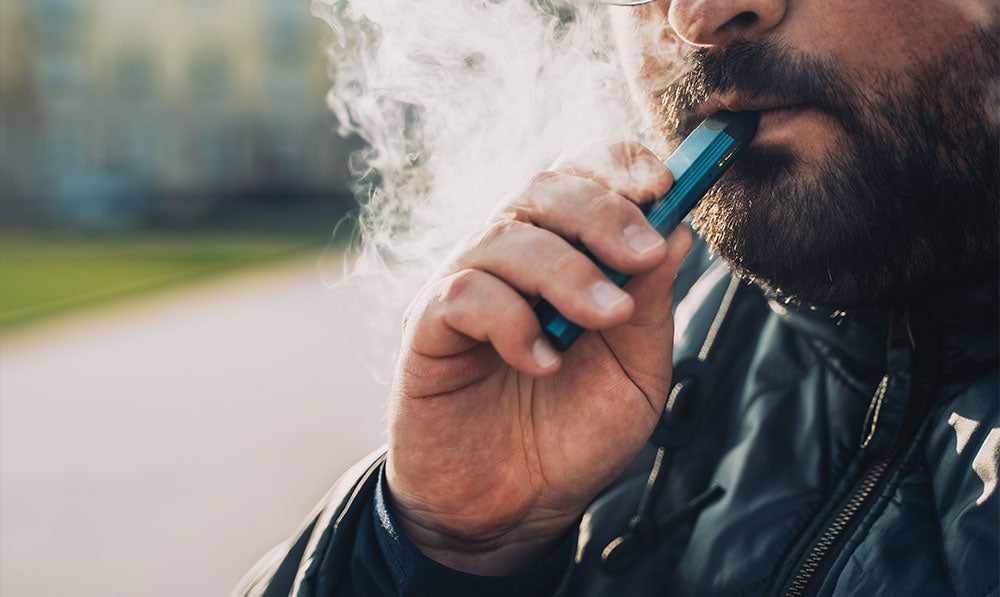 Man taking a mouth to lung draw from a vaporizer outside