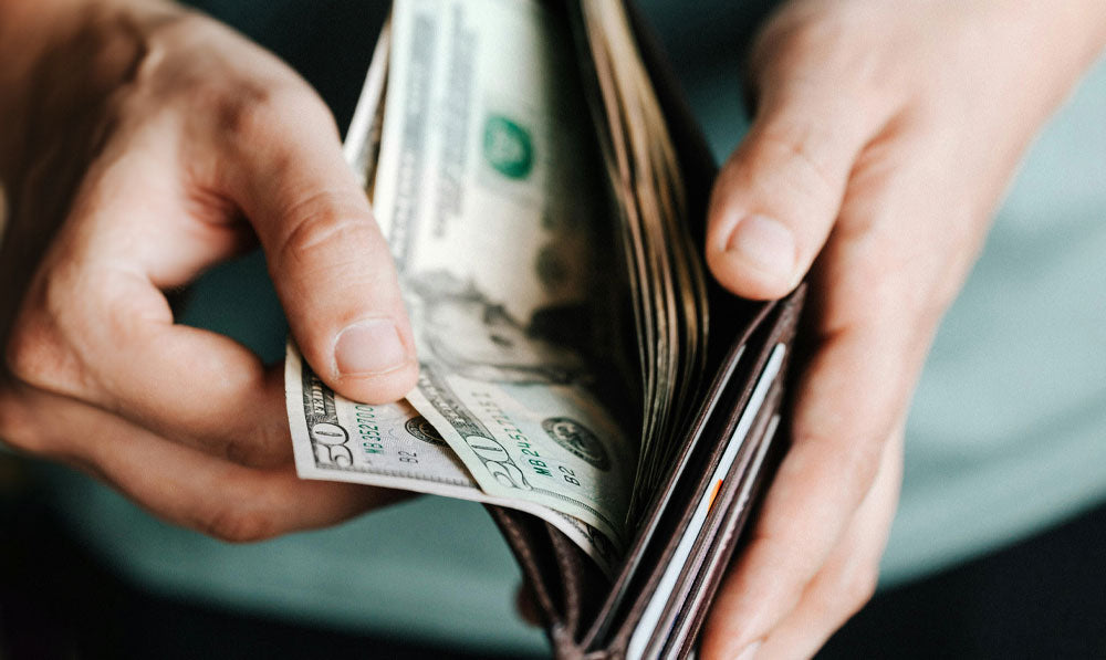 Two hands holding open a wallet with cash inside