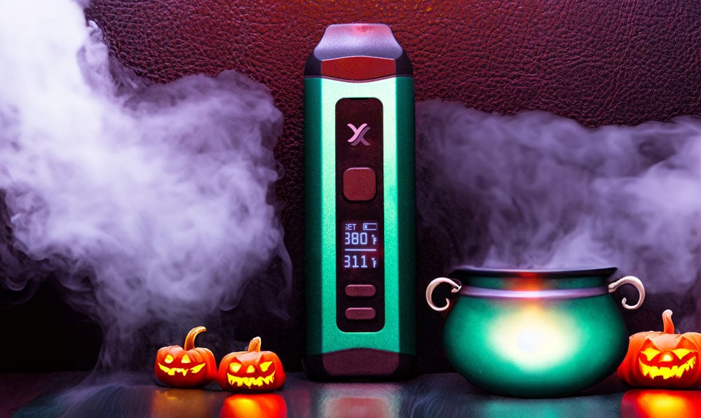 Exxus Mini Plus standing on dark surface with green cauldron and pumpkins