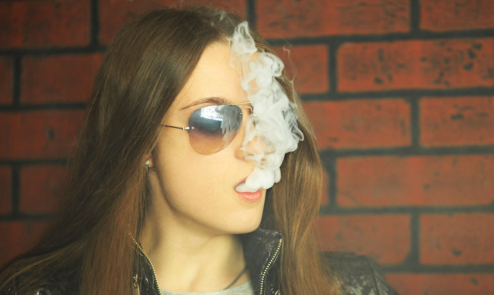 Woman in sunglasses vaping in front of brick wall
