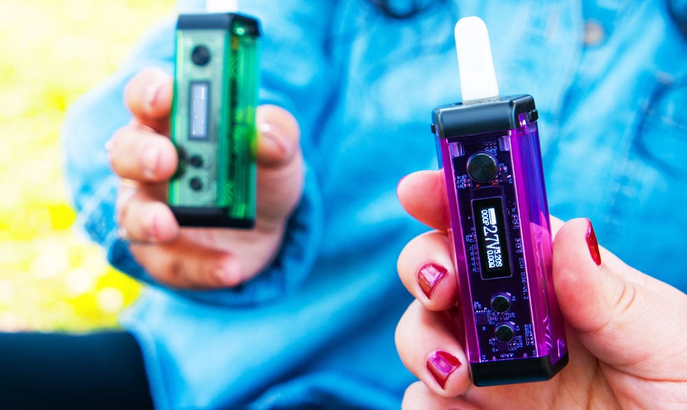 Two people holding Exxus Adapt vaporizers in a park