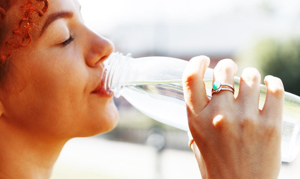 Redheaded woman drinking water outside