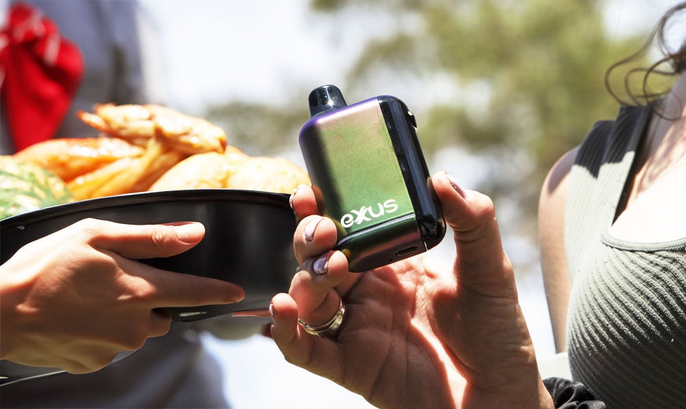 Woman holding Exxus Snap DLX while family member walks nearby with plate of food
