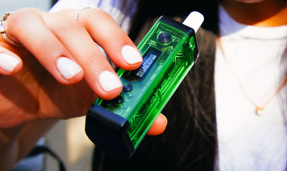 Person in a hat holding a green Exxus Adapt vaporizer