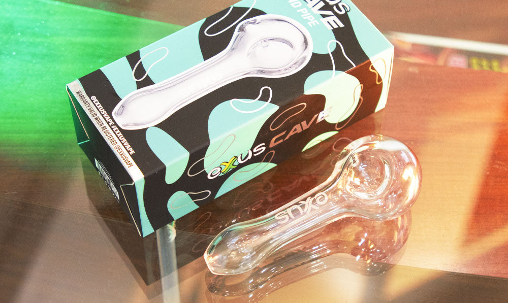 Exxus Cave glass hand pipe on a reflective surface with colourful backdrop