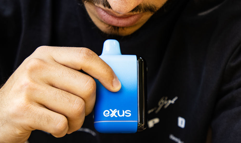 Hand holding a blue Exxus Snap DLX cartridge vaporizer with its magnetic cartridge door