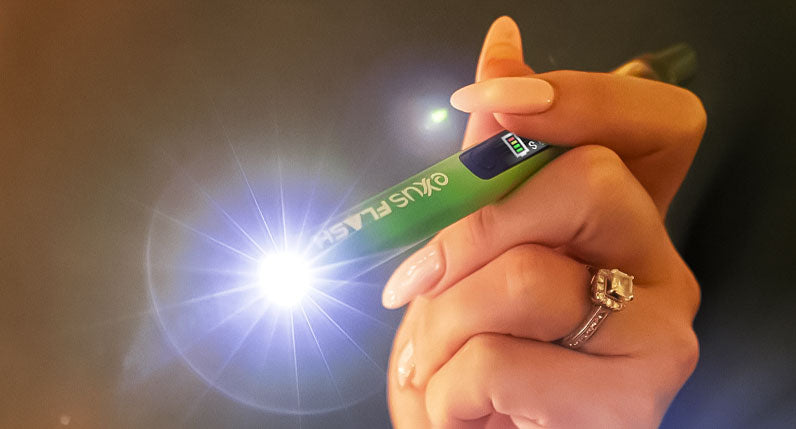 Hand holding a green Exxus Flash cartridge vaporizer with its flashlight lit